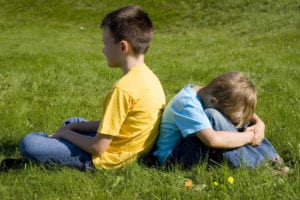 two boys sitting back to back in the grass, looking sad