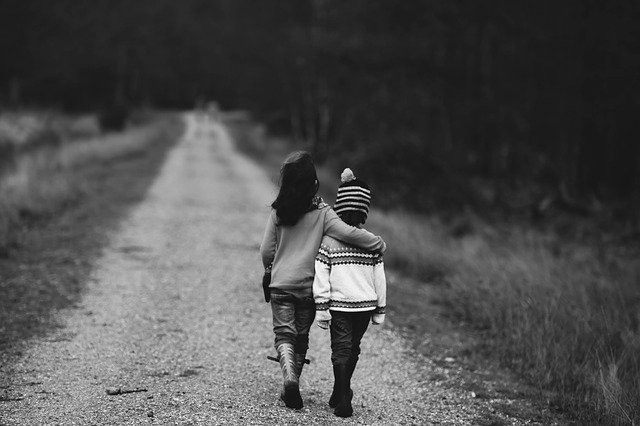 A black and white picture of two children walking arm in arm down a dirt road, away from the camera.