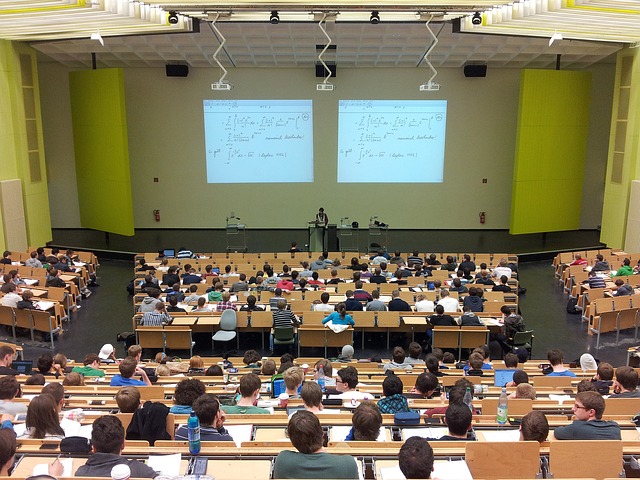 A picture of a lecture hall on a university campus, full of adult students all facing a college instructor.