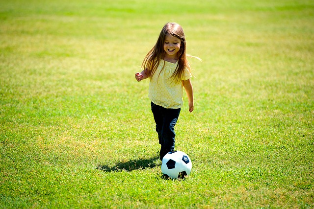 A young girl kicking a soccer ball on a field. She's having fun and laughing, but she is alone.