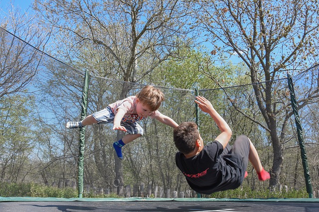 Two young boys jumping on a trampoline without an adult. They are probably too young to be left alone and without supervision.