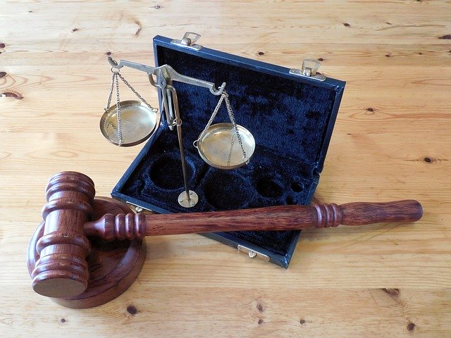 A Judge's hammer and a set of scales, representing the law, on a wooden table.