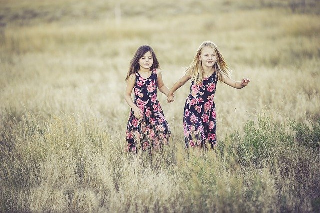 Two little sisters dressed in identical dresses holding hands and running through a field together.