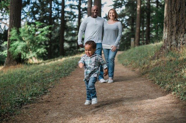 A couple walking down a path in the woods, with their young son running ahead of them and laughing
