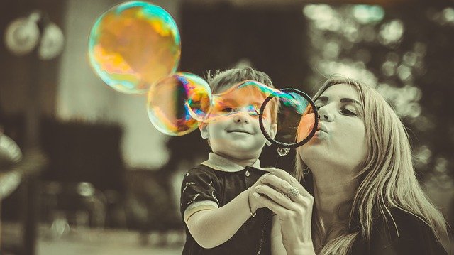 A mom and little boy blowing bubbles together and smiling.