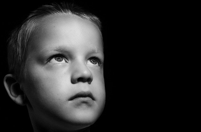 A little boy in a black and white picture looking up with a sad look on his face