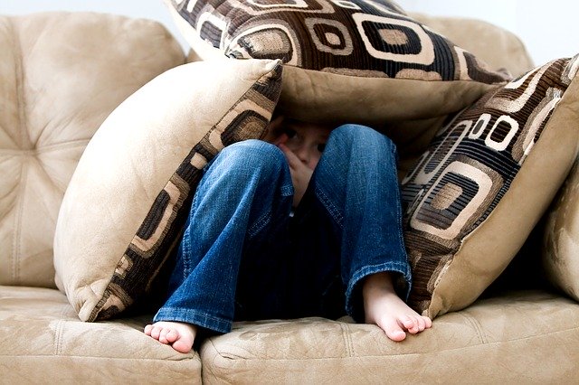 A child hiding under pillows on a couch.