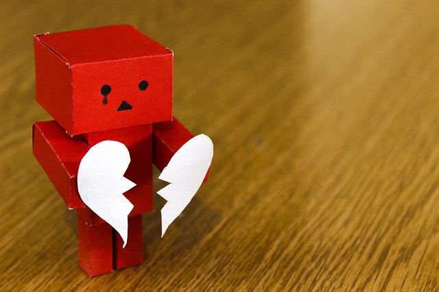 A little red paper robot holding the two pieces of a broken heart.