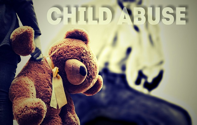 A child's hand holding a teddy bear, with an out of focus adult in the background. The words 'child abuse' are written across the top of the page.