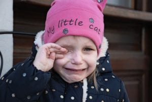 A crying girl wearing a pink hat and a blue coat