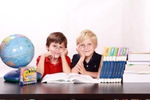 Two young boys with a globe, a stack of books, and crayons