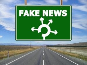 A sign hanging over a road showing the words "fake news" to imply that lies and falsehoods are ahead