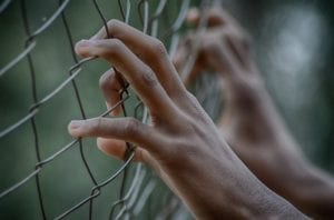 Hands grabbing a fence as if the person is trapped and wants out