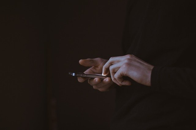 A person's hands, holding a cell phone and making a call in the dark, like a person making a mandatory report about suspected abuse.