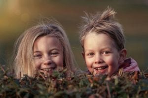 Two smiling children peeking over a hedge