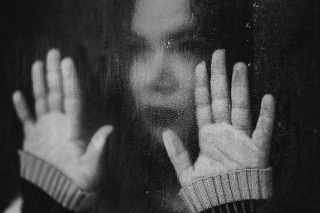 A black and white picture of a woman staring through a rainy window and looking sad.