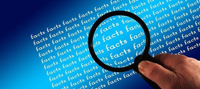 A person's hand holding a magnifying glass over the words 'facts' as if investigating.