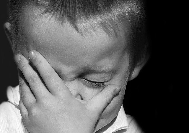 A black and white image of a young boy looking sad with his hand over his face.