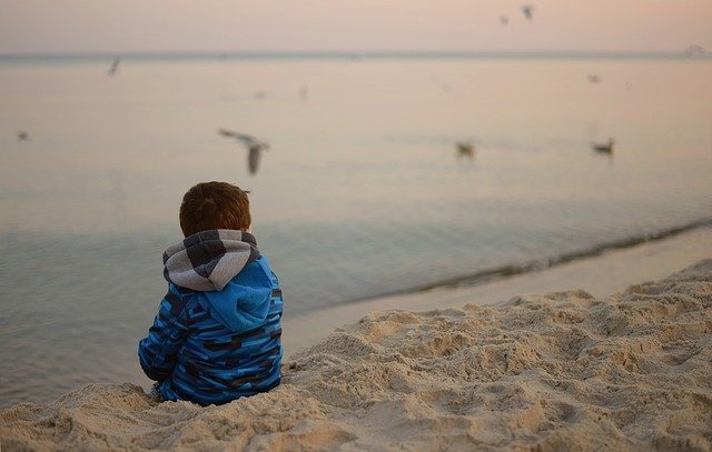 A child sitting alone on the beach with his back to the camera